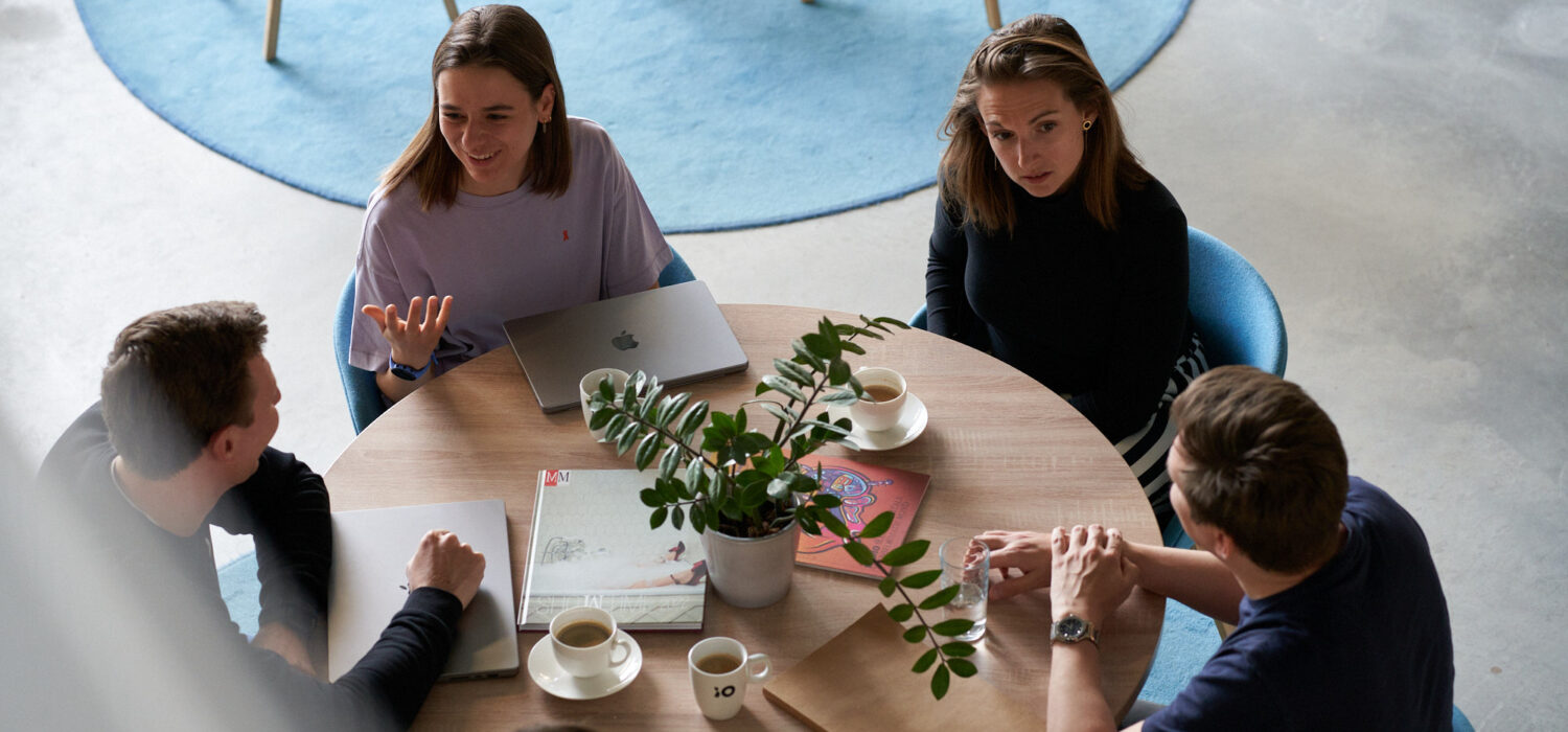 Två kvinnor och två män sitter vid ett runt bord och diskuterar