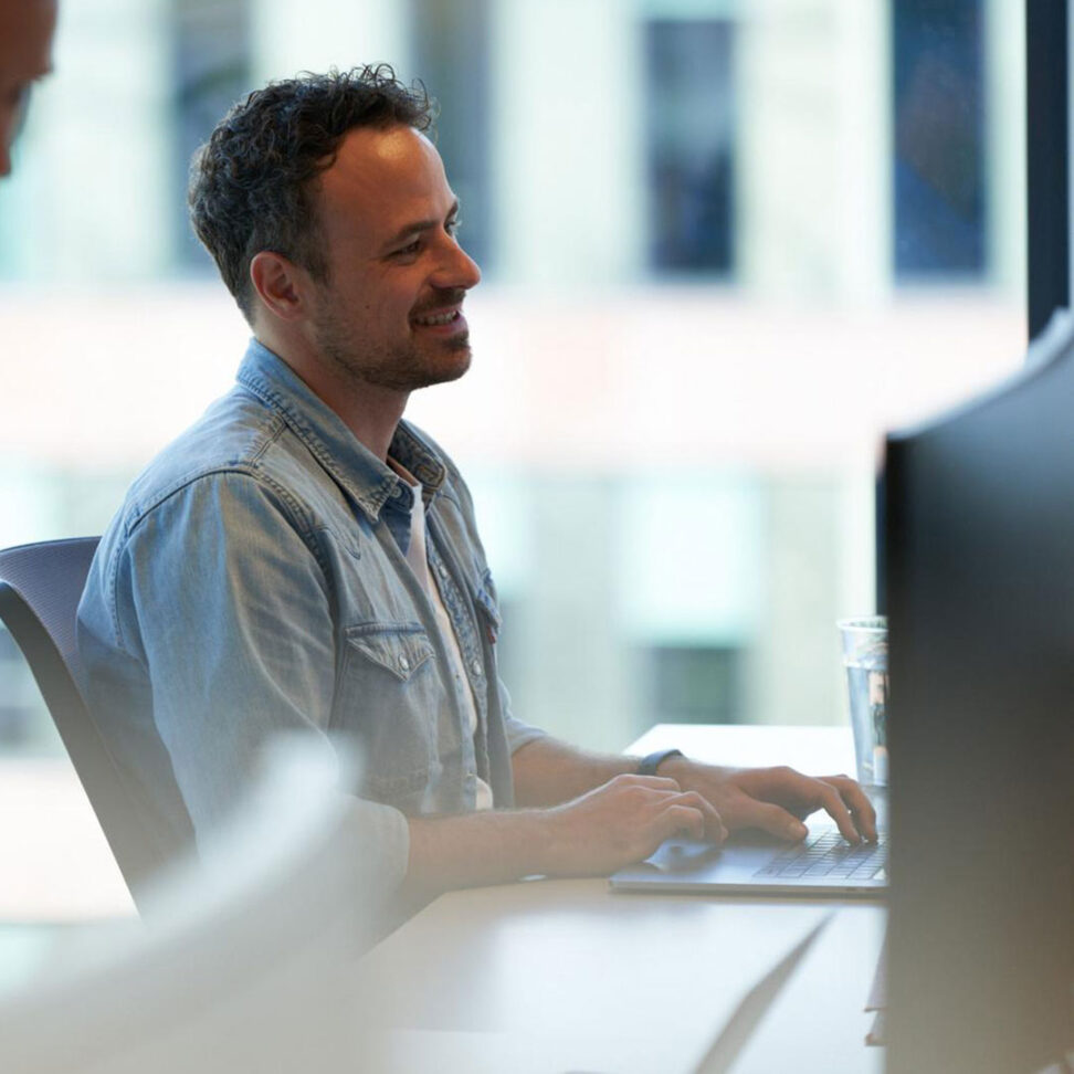 En man sitter vid en dator och ler