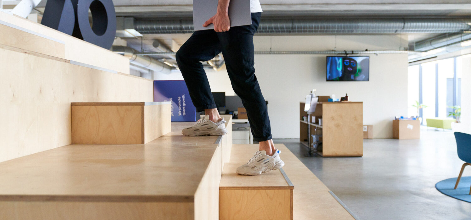 En person går uppför en trappa med en mobil i ena handen och en dator under andra armen